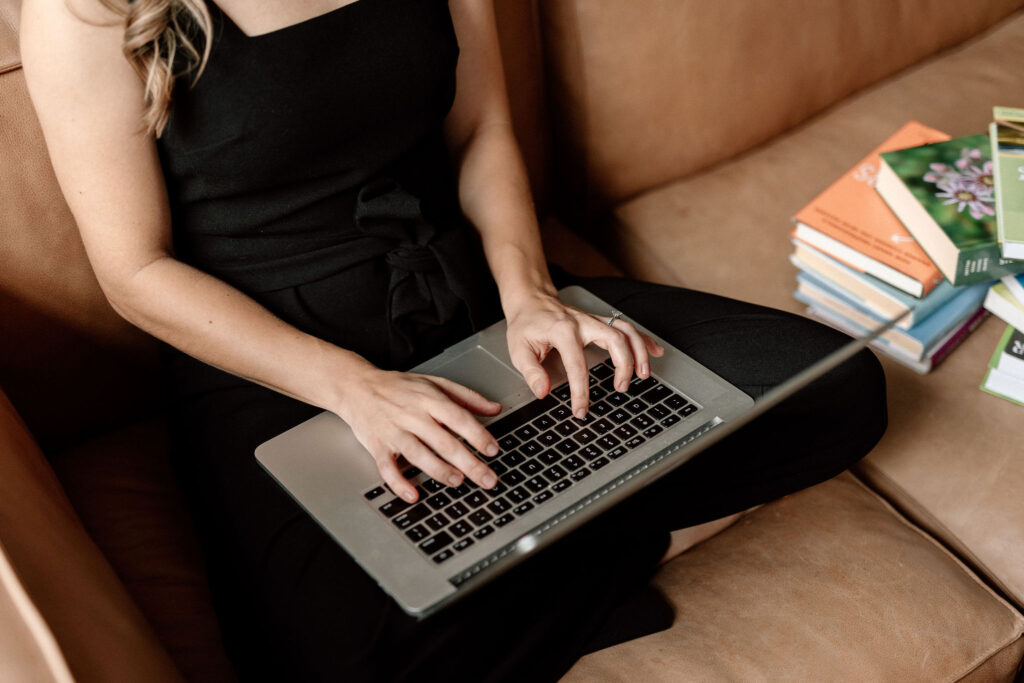 Entrepreneur Academic sharing when is the right time to create an online course on a leather couch wearing a black jumpsuit and working on a Macbook computer.